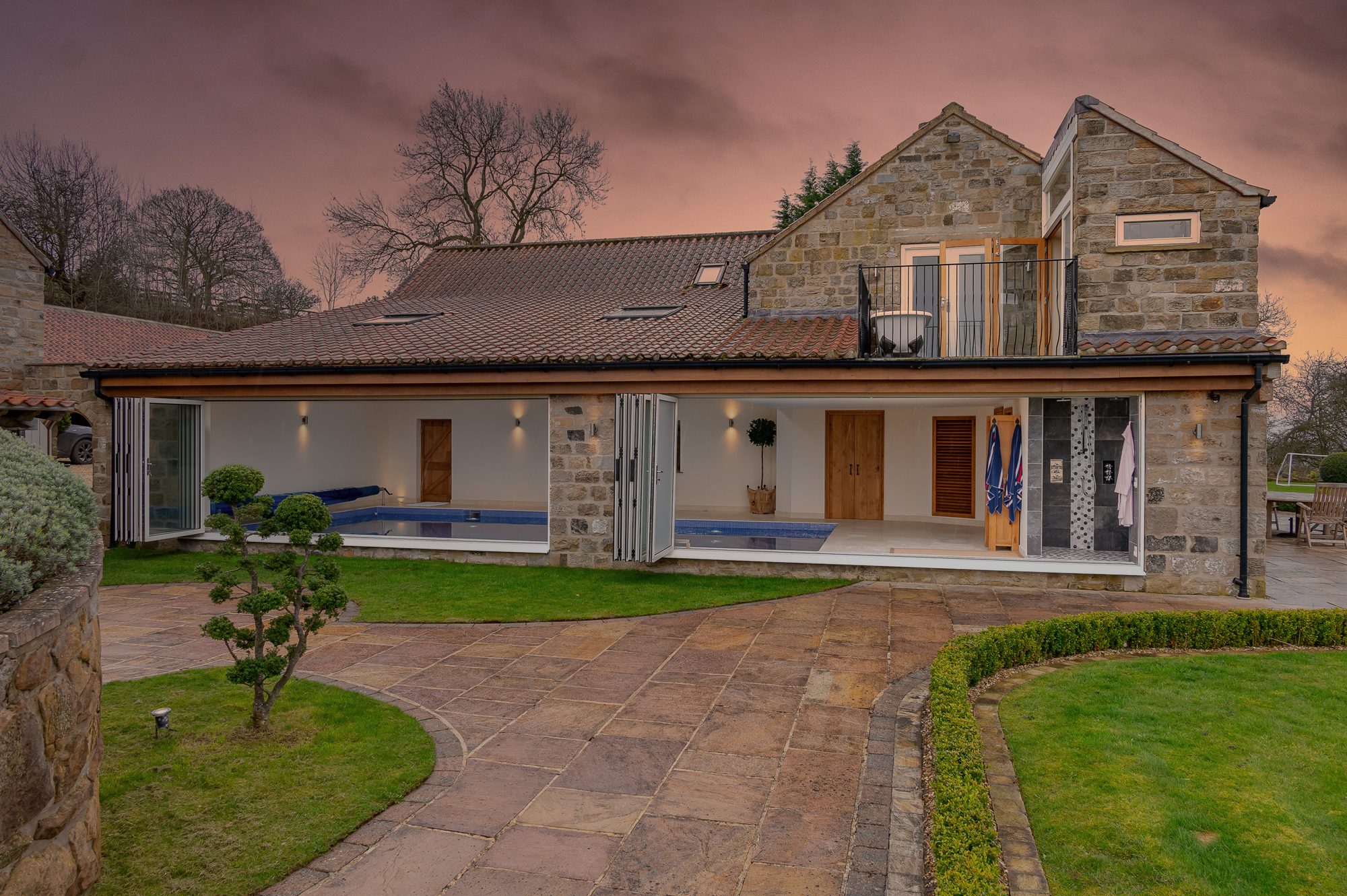 The pool wing lit up at dusk with the bi-fold doors open onto the garden